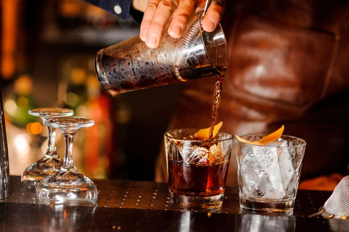 Barman pouring fresh alcoholic drink into the glasses with ice cubes on the bar counter