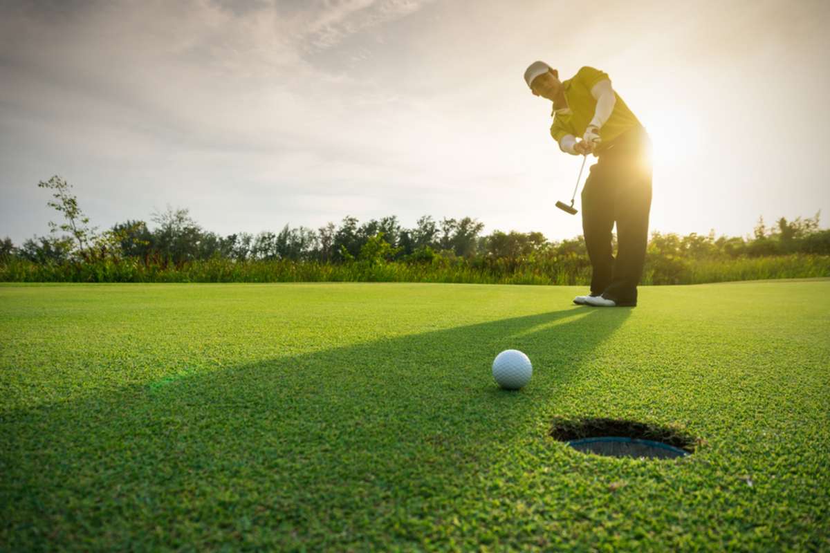 Golfer putting golf ball on the green golf, lens flare on sun set evening time