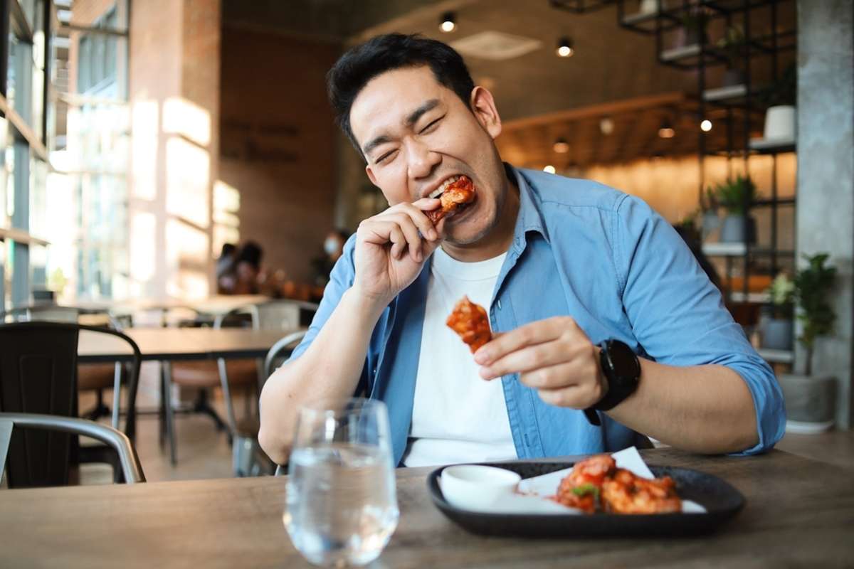 Happy Asian man eating BBQ chicken wings in restaurant