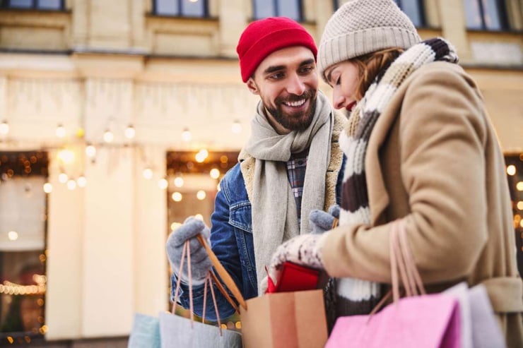 Happy young male is buying presents for beloved woman while they are walking in snowy street-1