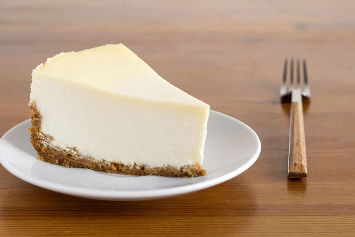 Slice of Plain New York Cheesecake on white plate on wooden background